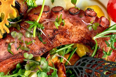 Beyaz bir masa örtüsünün üzerinde sebzeli ızgara ahtapot.