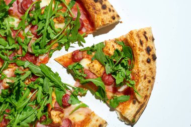 Beyaz arka planda salamlı, sosisli ve roka dilimlenmiş pizza.