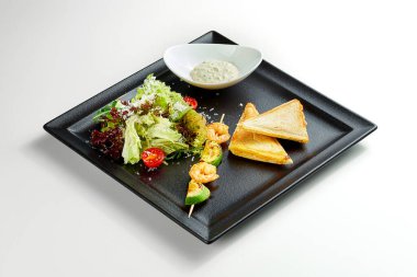 Peynirli ve karidesli kahvaltı tostu, gri arka planda siyah tabakta salata.