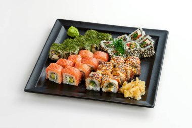 Gri arka planda siyah bir tabakta farklı rulolarla suşi seti. Somonlu rulo, yılan balığı