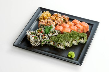 Gri arka planda siyah bir tabakta farklı rulolarla suşi seti. Somonlu rulo, yılan balığı