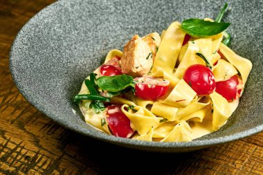 Beyaz soslu makarna, ahşap bir masada gri bir tabakta tavuk ve domates.