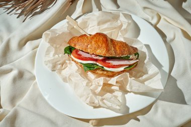Jambonlu, ıspanaklı ve domatesli kruvasan sandviç. Sert Işık. Beyaz masa örtüsü.