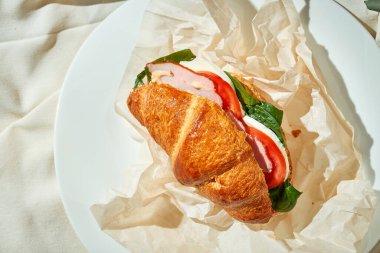 Jambonlu, ıspanaklı ve domatesli kruvasan sandviç. Sert Işık. Beyaz masa örtüsü.