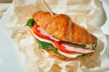 Jambonlu, ıspanaklı ve domatesli kruvasan sandviç. Sert Işık. Beyaz masa örtüsü.