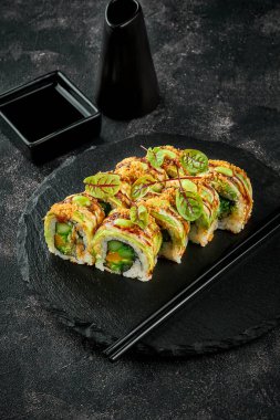 Siyah bir tabakta avokado, mango ve soslu vejetaryen suşi ruloları. Yakın plan.