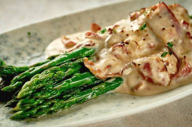 Asparagus with cream sauce and bacon on a plate. Close-up. Selective focus