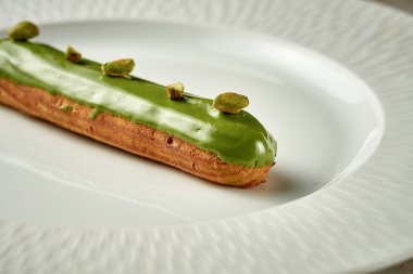 Eclair with pistachio glaze on a plate. Noise added in post-production. Selective focus