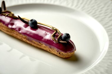 Eclair with berry glaze on a plate. Noise added in post-production. Selective focus
