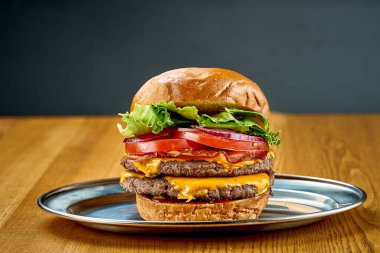 Domatesli, soğanlı, peynirli ve peynirli büyük sulu bir hamburger.