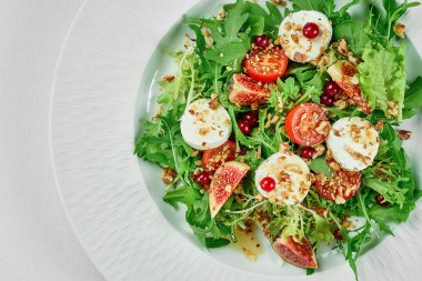 Keçi peynirli salata ve beyaz masa örtüsünde beyaz bir tabakta incir. Yakın çekim, seçici odaklanma