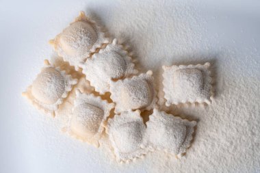 Ravioli makarna kareleri hafif arkaplanda un serpiştirilmiş..