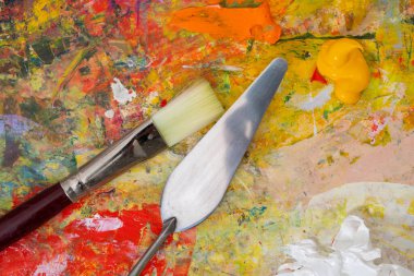 Renkli, karışık boyalar, palet bıçağı ve fırçayla yakın plan sanat paleti. Sanat konsepti