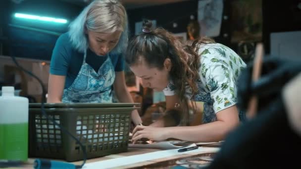 Dwie młode kobiety malarki omawiają i zbierają szczegóły witraża. Proces pracy. Witraż, rzemiosło. Ręcznie robione. — Wideo stockowe
