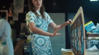 Sanatçı konuşur ve bitmiş vitray pencereye bir el hareketiyle gösterir. Arka planda, usta püre kullanıyor. Lekeli cam atölyesi. El işi, el işi. Tiffany tekniği. 