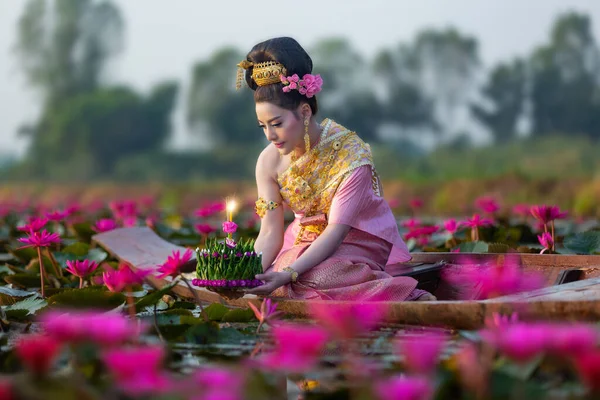 美丽的泰国女人 身穿泰国传统服装 躺在木船上 提着浮篮 Krathong 在泰国洛城的红莲湖中漂流 图库照片
