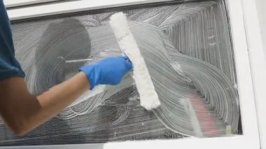 Tulumlu profesyonel erkek işçi, camları özel köpük ve ağır çekimde aletlerle temizleyip yıkamakla meşgul.