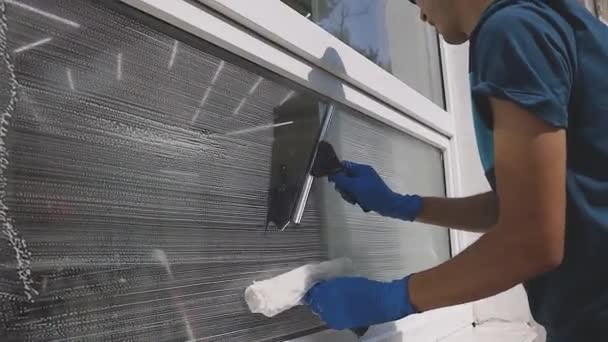 Професійний чоловік у комбінезоні займається прибиранням та миттям вікон за допомогою спеціальної піни та інструментів у повільному русі — стокове відео