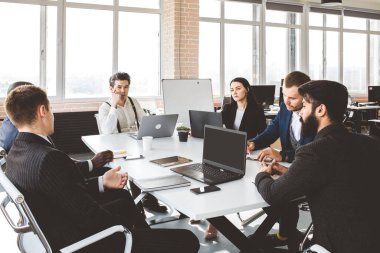 Ofis masasında iş arkadaşlarıyla otururken çalışan ve iletişim kuran bir grup genç iş adamı. iş toplantısı