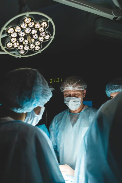 Une équipe internationale de chirurgiens, d'assistants et d'anesthésistes effectue une opération complexe sur un patient sous anesthésie générale. Thème de la photographie atmosphérique sombre en mode discret. — Photo