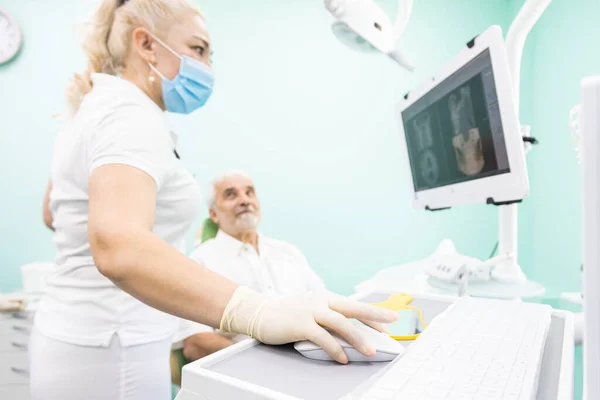 Odontologia e saúde. Serviços odontológicos profissionais e equipamentos modernos sem dor. O médico consulta um paciente idoso, olha para as fotos dos dentes na tela do monitor — Fotografia de Stock