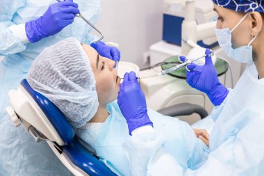 Dişçi konsepti. Profesyonel diş hizmetleri ve acısız modern ekipmanlar. Asistanı olan bir doktor hastaların dişlerini tedavi eder ve anestezi yapar.