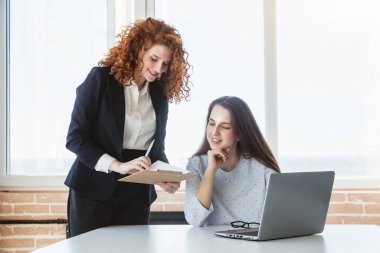 İki güzel genç kadın ofiste dizüstü bilgisayarla konuşuyor ve tartışıyorlar..