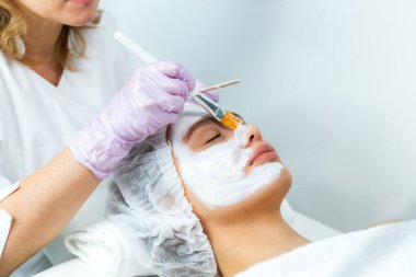 Yüz bakımı ve korunma. Güzellik uzmanıyla randevusu olan genç bir kadın. Uzman yüzüne krem maske takıyor.