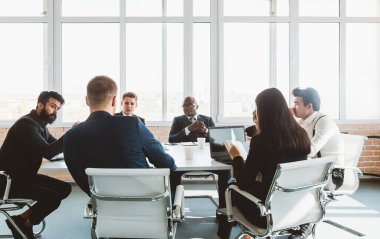 Ofis masasında iş arkadaşlarıyla otururken çalışan ve iletişim kuran bir grup genç iş adamı. iş toplantısı