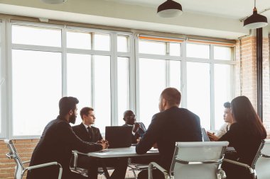 Ofis masasında iş arkadaşlarıyla otururken çalışan ve iletişim kuran bir grup genç iş adamı. iş toplantısı