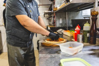 Mutfakta pizza kesen beyaz üniformalı aşçının yakın çekimi.