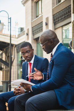 Açık havada iki Afro-Amerikan işadamının dostça buluşması. Ortaklar bankta oturup ortak bir projeyi tartışırlar.
