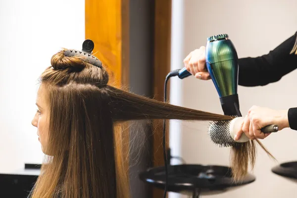 Mester nő fodrász szárítja a lányok haját egy hajszárítóval és fésülködik mosás után a szépségszalonban — Stock Fotó