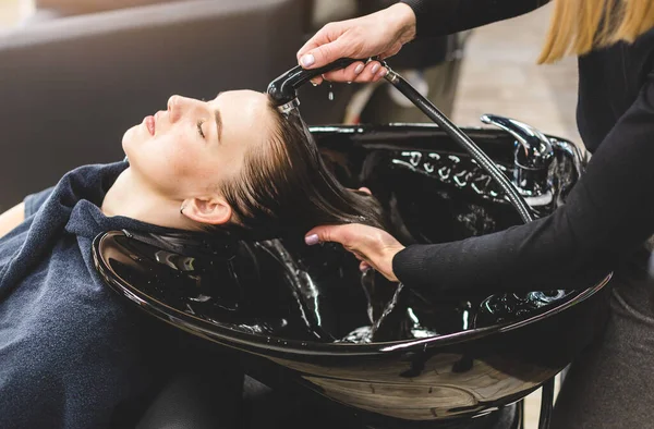 Friseurmeisterin wäscht die Haare der Mädchen sanft mit Shampoo und Conditioner, bevor sie sich in einem Schönheitssalon stylt. — Stockfoto