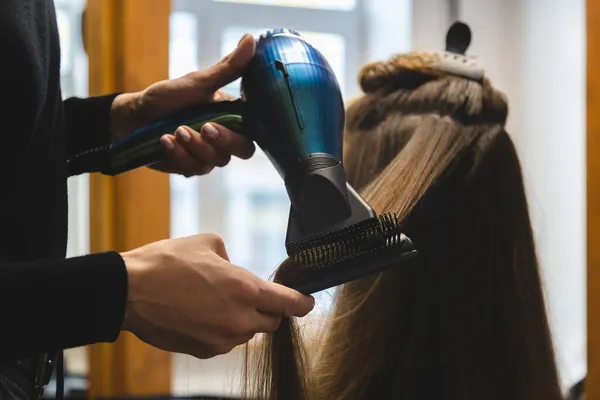 Maestra mujer peluquería seca el pelo de las niñas con un secador de pelo y peines después de lavarse en el salón de belleza — Foto de Stock