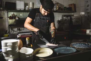 Oteldeki mutfak restoranında yemek pişiren profesyonel bir aşçı. Yemek hazırlıyor. Önlüklü bir aşçı sebze ve pizzadan salata yapar. Gösterişsiz ışıklandırma