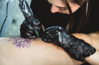 Profesyonel kadın dövme sanatçısı stüdyoda dövme yapıyor, yakın plan. Karanlık fotoğrafçılık