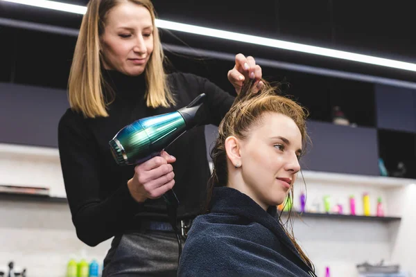 Master parrucchiere donna asciuga i capelli delle ragazze con un asciugacapelli dopo il lavaggio in un salone di bellezza. — Foto Stock