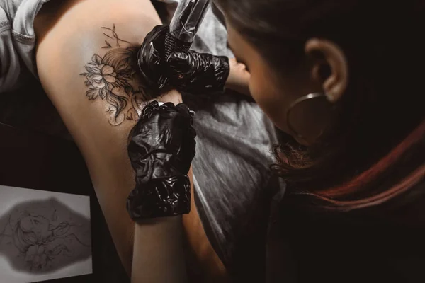 Dessin d'un tatouage sur la jambe gros plan. Femme tatoueuse fait un dessin avec une machine spéciale dans un studio d'art — Photo
