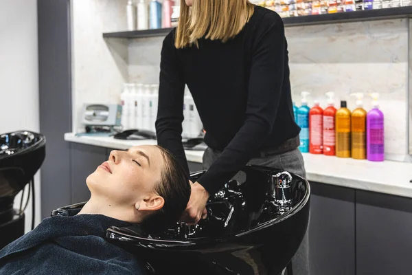Master parrucchiere donna lava delicatamente i capelli delle ragazze con shampoo e balsamo prima di styling in un salone di bellezza. — Foto Stock