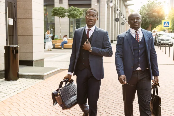 Deux hommes d'affaires afro-américains à la peau foncée en costume avec mallettes marchent le long de la rue de la ville — Photo