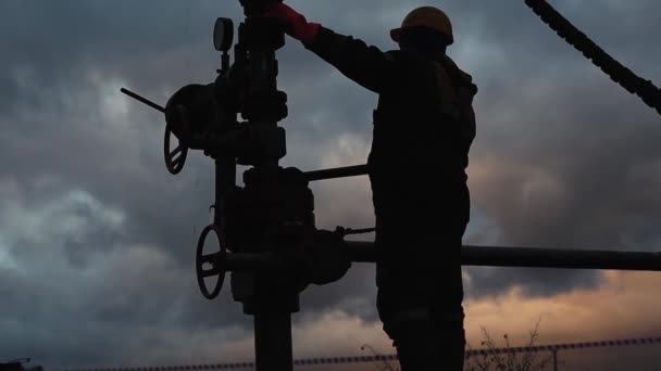Zaměstnanec v montérkách a helmě provádí opravy a údržbu ropné vrty. Silueta na pozadí večerní oblohy — Stock video