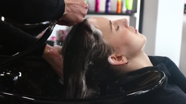 Cabeleireiro mulher mestre lava o cabelo de uma menina com shampoo antes de styling em um salão de beleza. — Vídeo de Stock