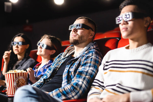 Friends are watching a movie in the cinema. People sit in the armchairs of the cinema and look at the screen with special glasses for 3D