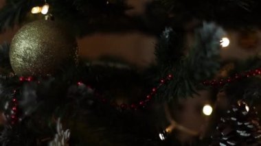 Noel ağacının dallarındaki Noel süslemeleri, arka plandaki çelenk ışıklarının sıcak ışıklarıyla titreşiyor..