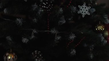 Noel ağacının dallarındaki Noel süslemeleri, arka plandaki çelenk ışıklarının sıcak ışıklarıyla titreşiyor..