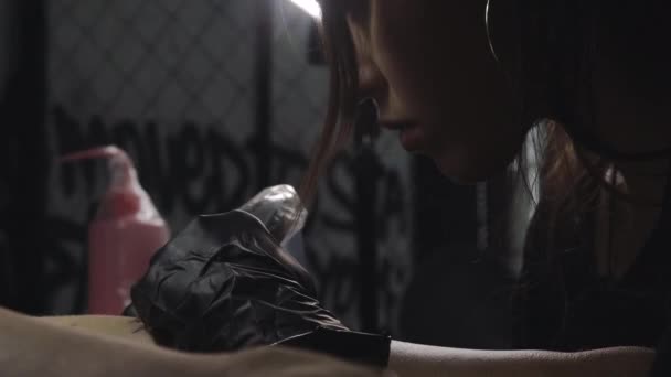 Ein professioneller Tätowierer fertigt eine schwarz-weiße Tätowierung auf einem Frauenbein an, die er mit Tinte aufträgt. Der Prozess der Tätowierung der Haut. — Stockvideo