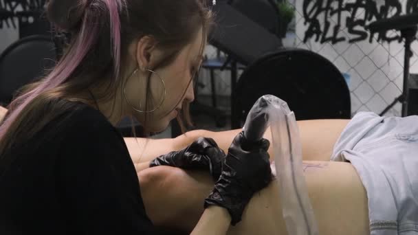 Profesjonalny tatuażysta robi czarno-biały tatuaż na kobiecej nodze, stosując atrament. Proces tatuażu na skórze. — Wideo stockowe