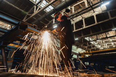 Bir fabrika işçisi, bir üretim hangarının zeminine karşı koruyucu bir maske takan kaynak makinesiyle metal kaynak yapıyor..