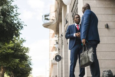 Takım elbiseli iki siyahi Afro-Amerikan işadamının portresi dışarıda el sıkışıyor. İyi arkadaşlarla tanışmanın sevinci